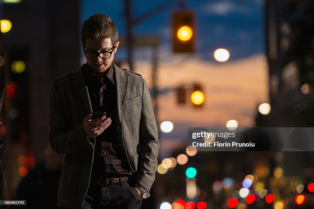 Young man strolling down street looking at mobile phone, Toronto, Ontario, Canada