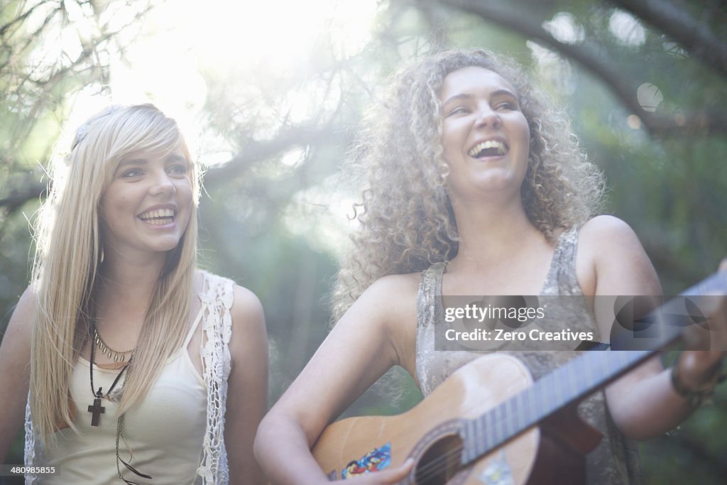 Two teenage girls playing guitar in woodland