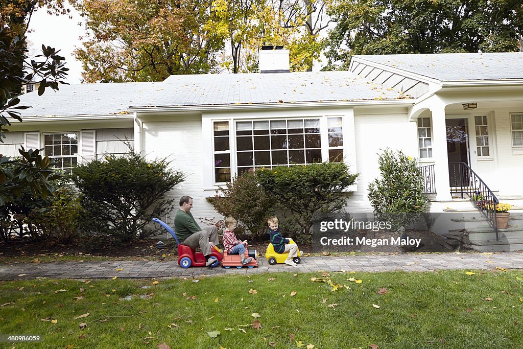 Father and young sons riding on toy cars in garden