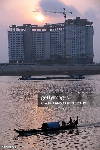 Boat sails as the sun rises over a hotel building under construction in Phnom Penh on March 28, 2014. The Southeast Asian nation, written off as a...