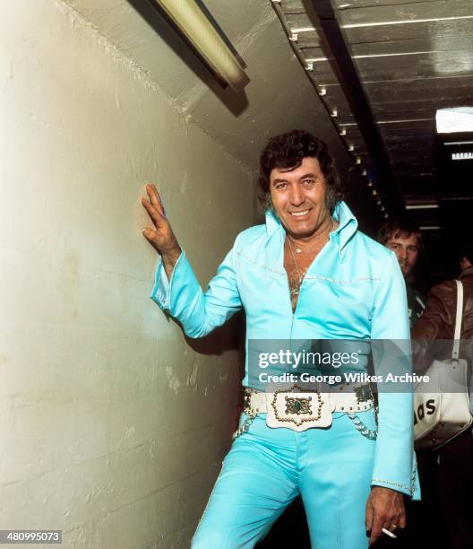 Portrait of American rockabilly musician Carl Perkins , dressed in a powder-blue jumpsuit, as he poses backstage, London, England, 1970.