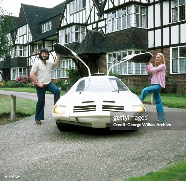 British disc jockey Dave Lee Travis and his wife, Marianne Griffin, pose together, each with one leg in the open, gull-wing style doors of their...