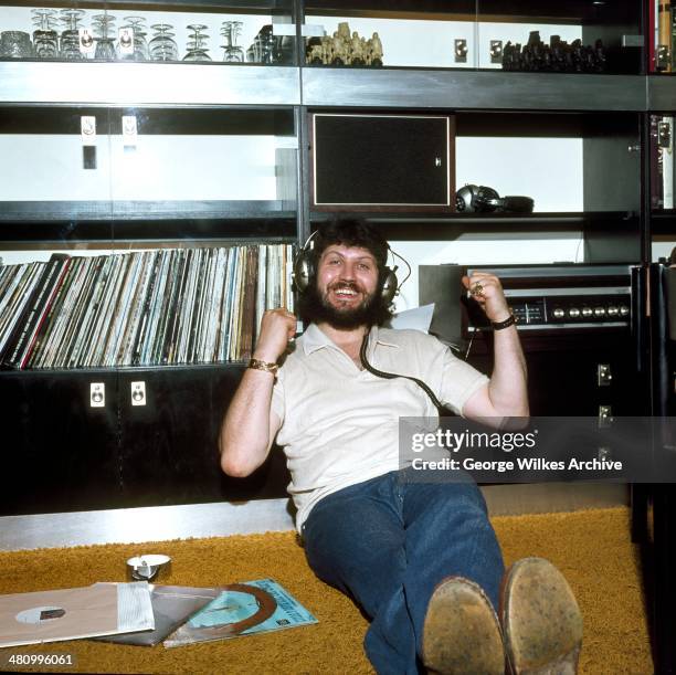 British disc jockey Dave Lee Travis listens to music on his headphones at home, London, England, 1973.