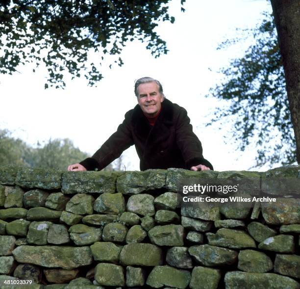 Portrait of English actor Ian Carmichael, OBE as he leans over the top of a wall, London, England, 1975.