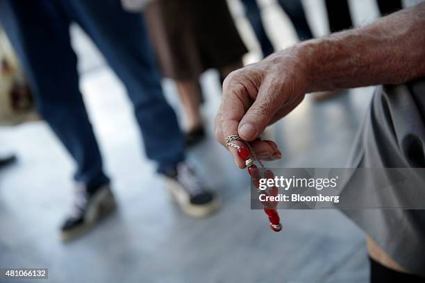 Pensioner plays with worry beads as he waits to enter a National Bank of Greece SA bank branch to collect his pension in Athens, Greece, on Friday,...