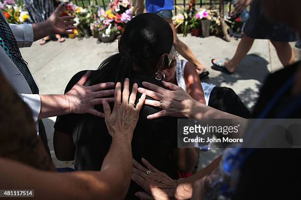 Visiting members of the Order of St. Luke bless a woman in front of the Emanuel AME Church on the one-month anniversary of the mass shooting on July...