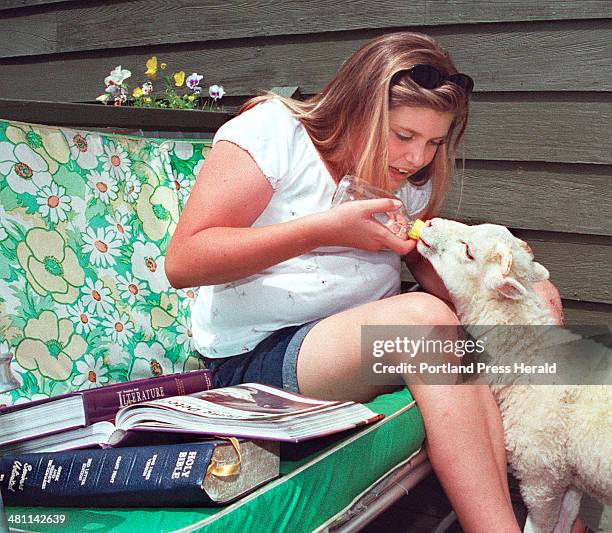 Staff Photo by Gordon Chibroski, Friday, June 30, 2000: Lindsay Nickerson takes a break from her studies at home to feed water to her lamb, part of...