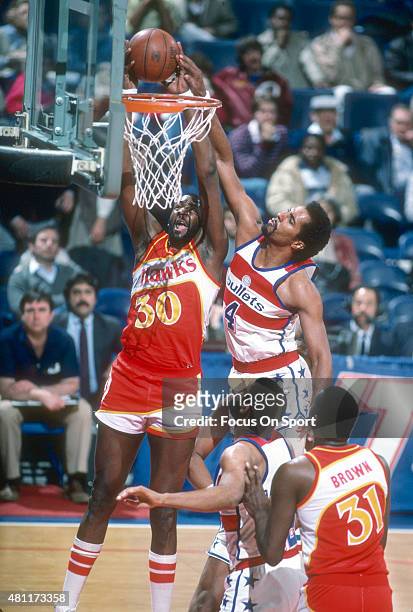 Wayne Rollins of the Atlanta Hawks goes up to slam dunk the ball over Cliff Robinson of the Washington Bullets during an NBA basketball game circa...