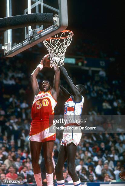 Wayne Rollins of the Atlanta Hawks has his shot blocked by Manute Bol of the Washington Bullets during an NBA basketball game circa 1987 at the...