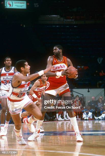 Wayne Rollins of the Atlanta Hawks looks to pass the ball over Jeff Malone of the Washington Bullets during an NBA basketball game circa 1987 at the...