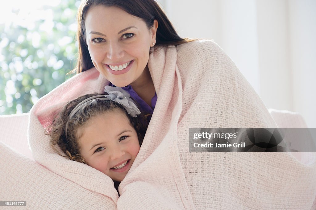 Mother and daughter cuddling under blanket