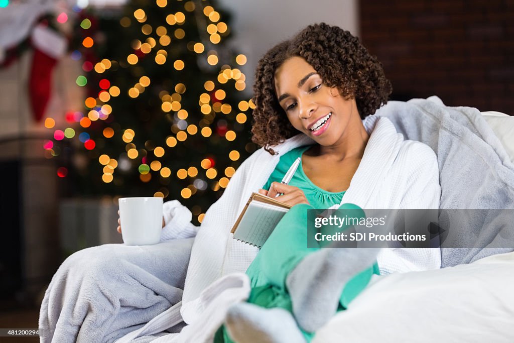 African American woman writing in journal while relaxing Christmas morning