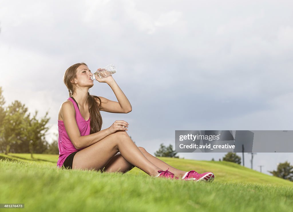 Fitness Mädchen Trinkwasser Sitzen im Park