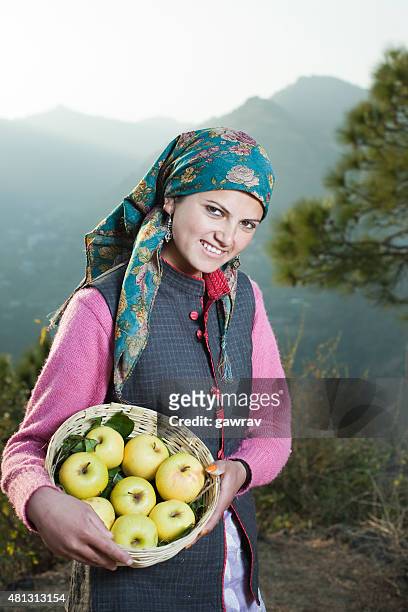 rural woman holding apple basket looking at camera in mountains. - himachal pradesh stock pictures, royalty-free photos & images