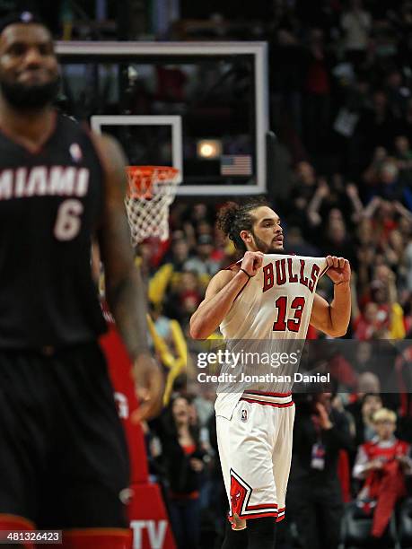 Joakim Noah of the Chicago Bulls pulls on his jersey in celebration as LeBron James of the Miami Heat walks down the court at the United Center on...