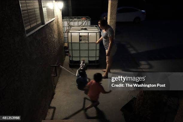 Paula Garcia, with son Michael checks the level of non-potable water in containers that were recently placed in front of their home in Porterville,...