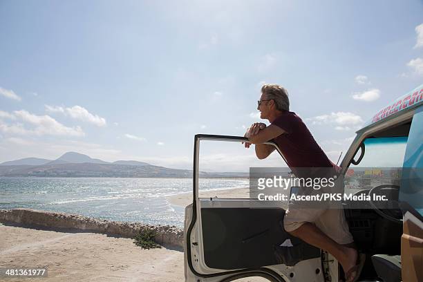 man leans across van door, looks out across sea - vehicle door stock pictures, royalty-free photos & images