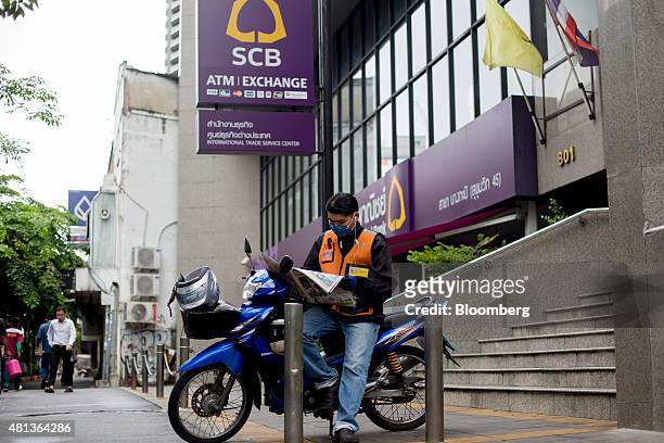 Motorcycle taxi driver reads a newspaper outside a Siam Commercial Bank Pcl branch in the Sukhumvit area of Bangkok, Thailand, on Monday, July 21,...