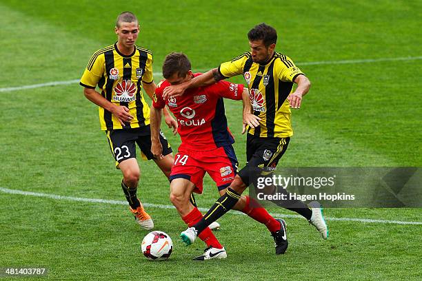 Cameron Watson of Adelaide United is tackled by Vince Lia of the Phoenix while Matthew Ridenton looks on during the round 25 A-League match between...