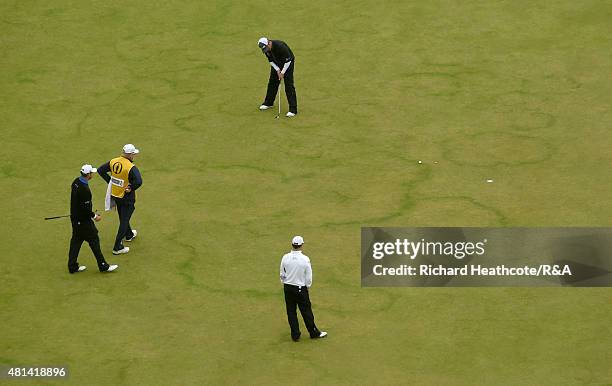 Louis Oosthuizen of South Africa holes a birdie putt on the first hole as Marc Leishman of Australia and Zach Johnson of the United States look on...