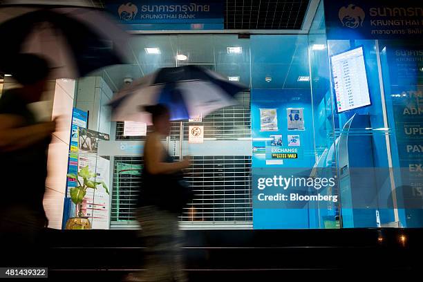 Pedestrians holding umbrellas walk past a Krung Thai Bank Pcl branch at night in the Silom area of Bangkok, Thailand, on Monday, July 20, 2015. Krung...