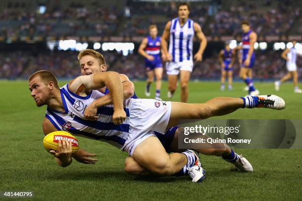 Leigh Adams of the Kangaroos handballs whilst being tackled by Lachie Hunter of the Bulldogs during the round two AFL match between the Western...