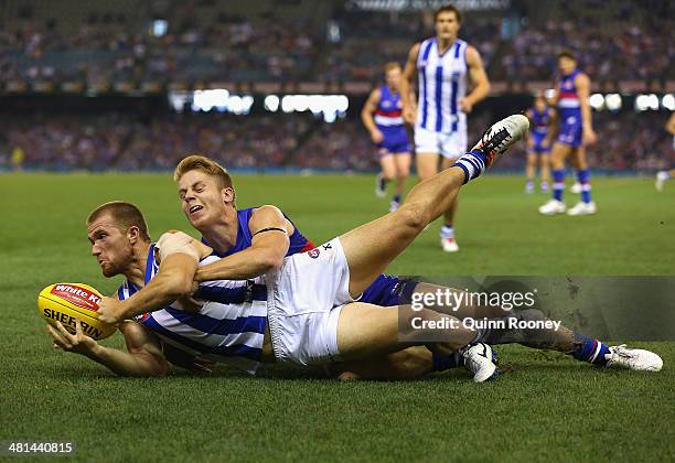 Leigh Adams of the Kangaroos handballs whilst being tackled by Lachie Hunter of the Bulldogs during the round two AFL match between the Western...