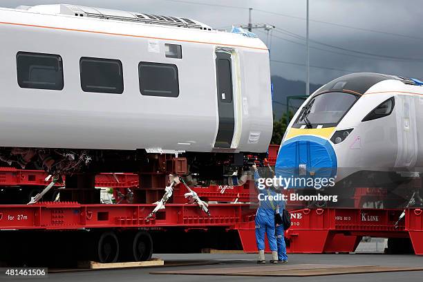 Workers check a Class 800 Intercity Express train railcar, manufactured by Hitachi Ltd., while it sits with another as they wait to be loaded onto a...