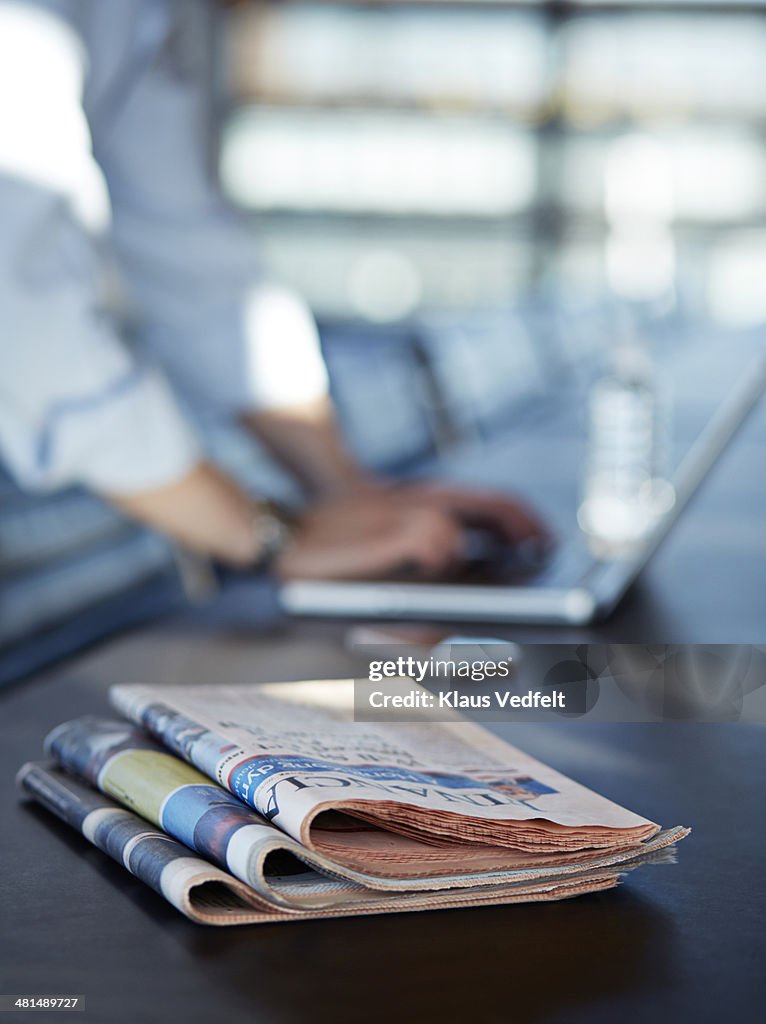 Close-up of newspapers & hands writing on laptop