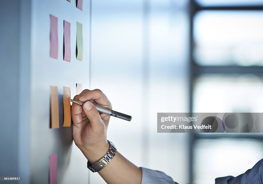 Hand writing on colorful Post-It notes on wall