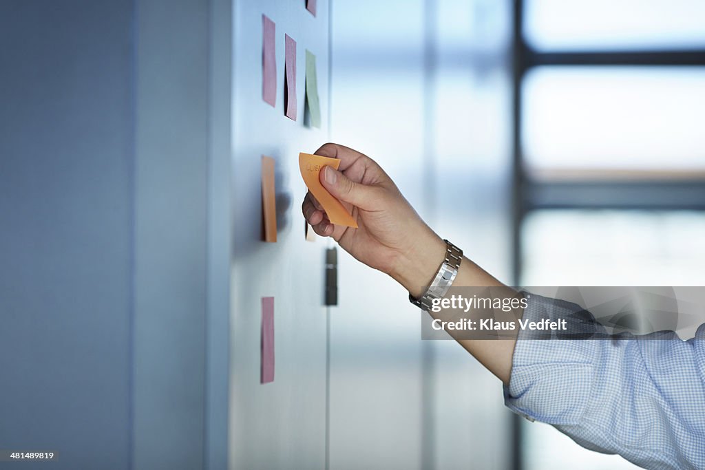Hand writing on colorful Post-It notes on wall