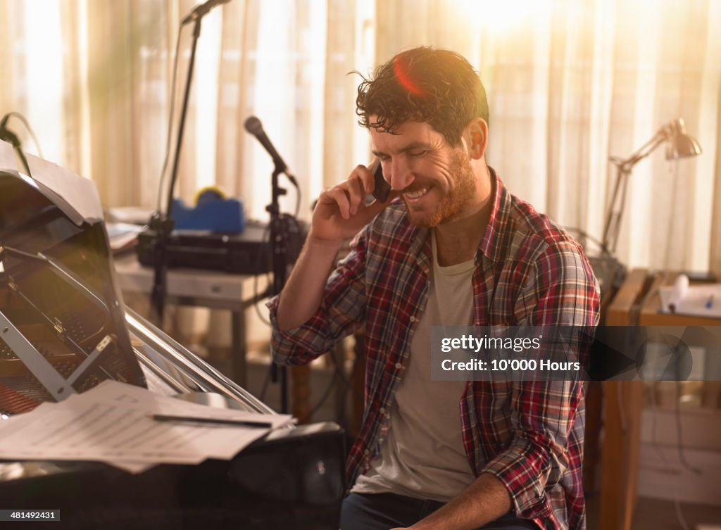 Young man sitting at a piano on the phone, smiling