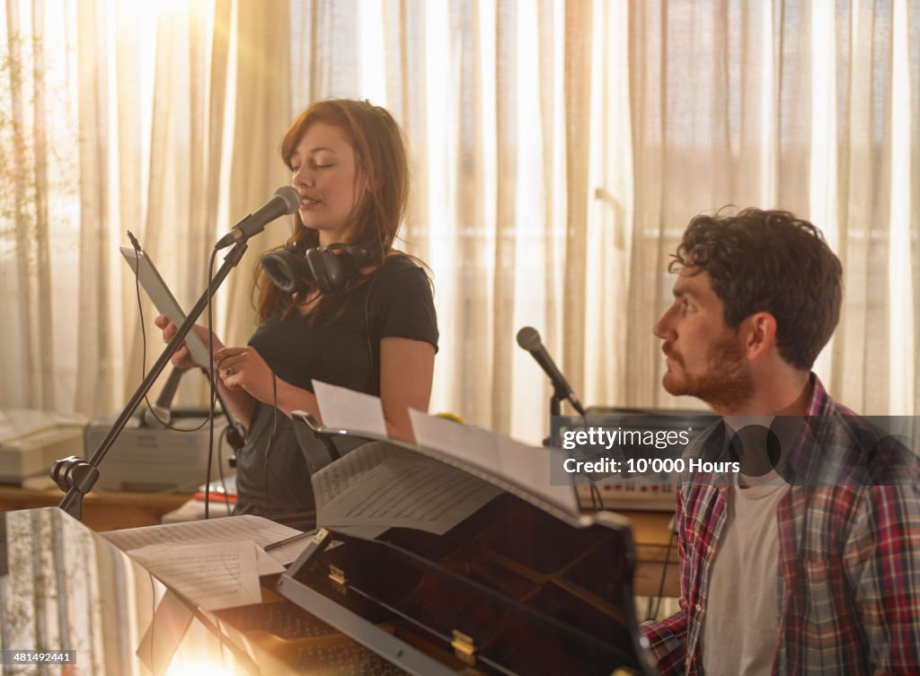 Man at piano, woman singing holding tablet compute