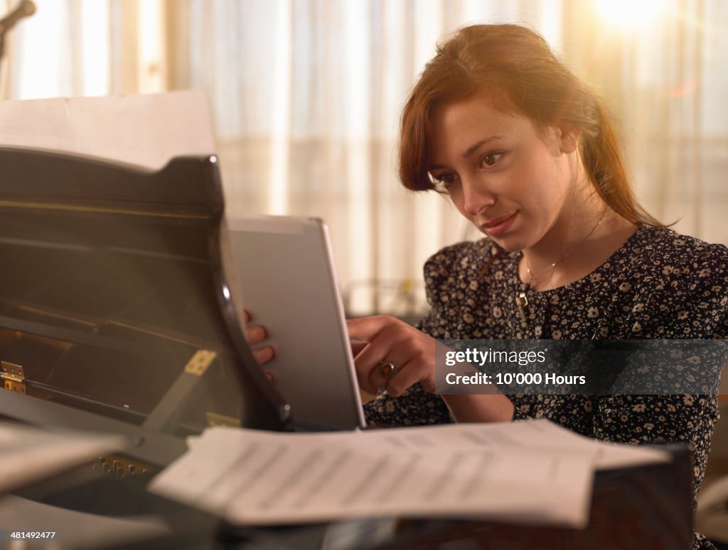 Young woman sitting at piano using tablet computer