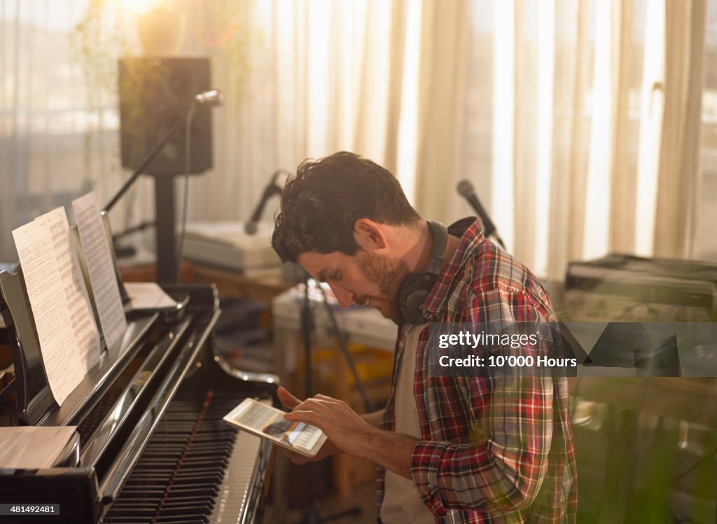Man sitting at grand piano using an tablet computer