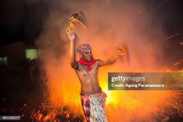 Balinese man swings his hands as he hold burned coconut husks during the "Mesabatan Api" ritual a head of Nyepi Day on March 30, 2014 in Gianyar,...