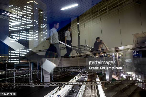 Office workers are seen reflected in a window as they walk to a train station in front of the Toshiba Corporations, Tokyo headquarters on July 22,...