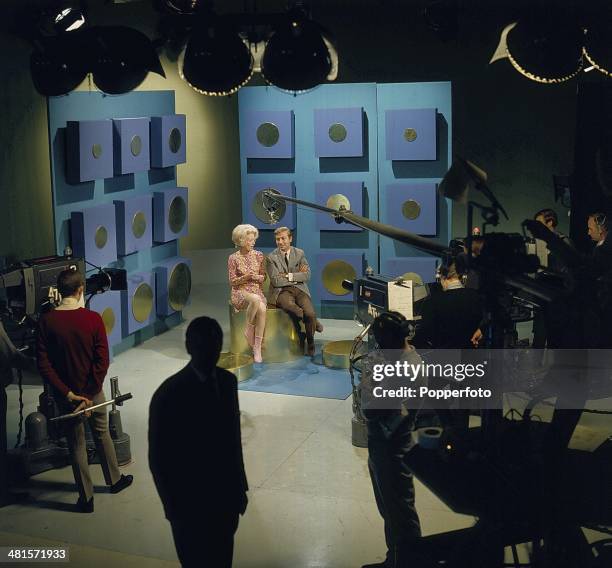 Wide view of a television studio featuring English singer and presenter Des O'Connor posed with a guest on the set of the television series 'the Des...