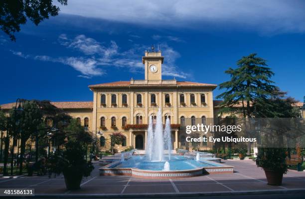 Italy, Emilia Romagna, Cattolica, Elegant yellow town hall building with trees and a fountain in the foreground.