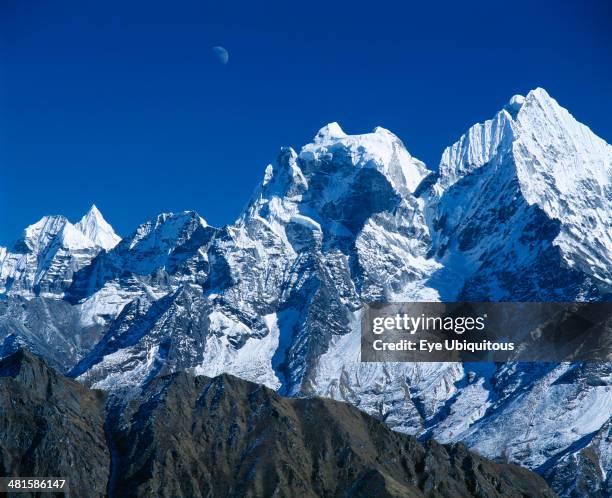 Nepal, Sagarmatha National Park, Himalayan mountain peaks with moon above just visible in deep blue sky.