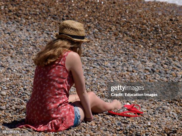 Teenage girl sat on the beach, Seaton, Devon, UK.