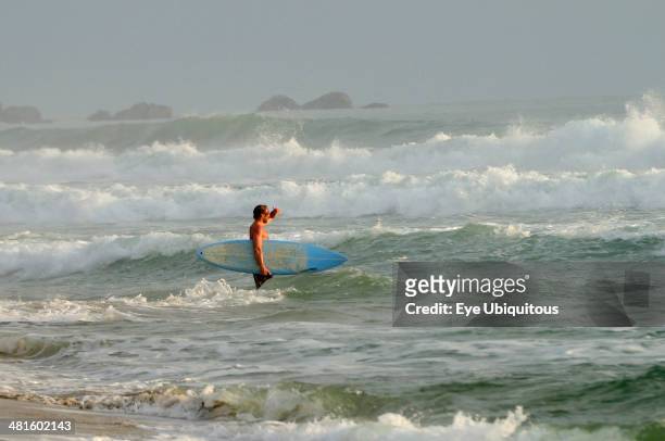 Mexico, Oaxaca, Puerto Escondido, Surfer walking through surf carrying board.