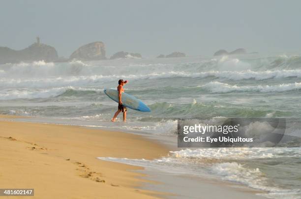Mexico, Oaxaca, Puerto Escondido, Surfer walking into surf carrying board.
