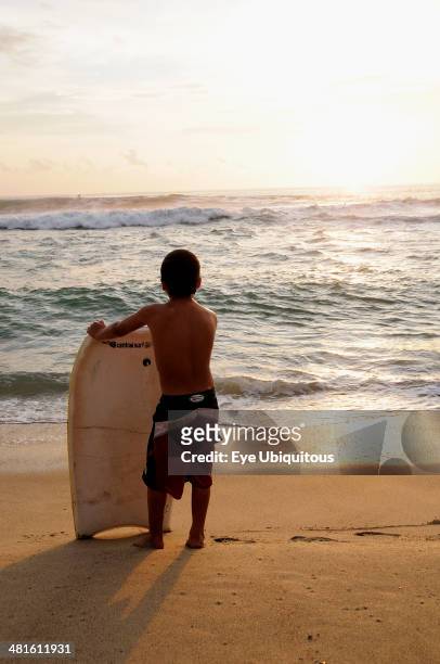 Mexico, Oaxaca, Puerto Escondido, Playa Zicatela Young body boarder standing on beach looking out to sea.