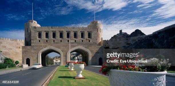 Oman, Muscat, Muscat Gate Museum, Crenellated gatehouse with archways over roads divided by central strip of grass with white tubs of red and white...