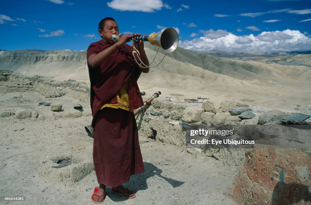 Tibetan Buddhist monk blowing horn on monastery roof to summon the faithful to prayer
