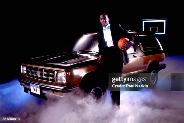 Portrait of professional basketball player Michael Jordan, of the Chicago Bulls, dressed in a tuxedo with a basketball under one arm as he poses with...
