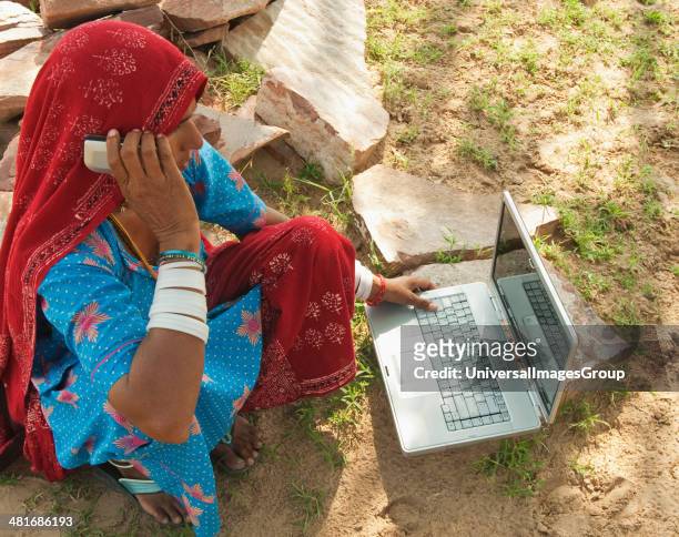 Rural woman talking on a mobile phone and using a laptop, Jaipur, Rajasthan, India.