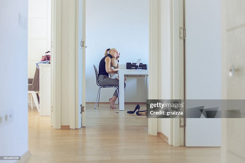 Woman working at laptop with baby in her arms