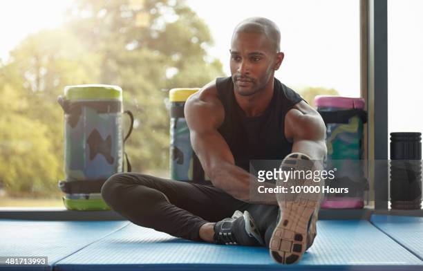a man stretching his hamstrings in the gym - adult male vest exercise stock pictures, royalty-free photos & images